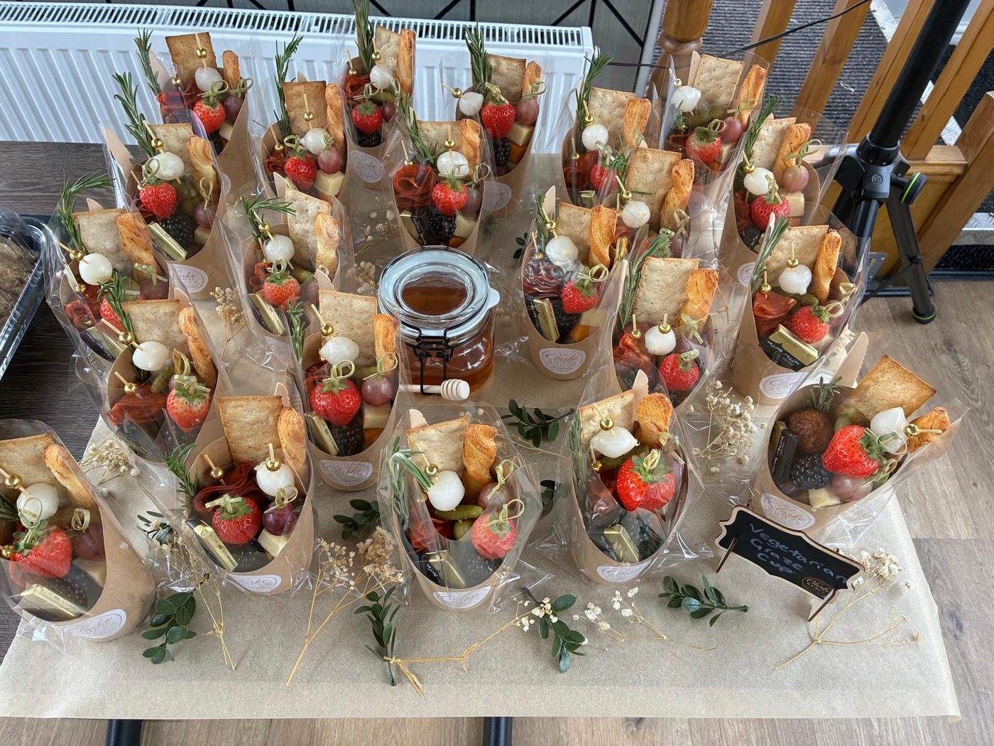 Individual grazing cones filled with meats, cheese, crackers and strawberries, with a jar of honey