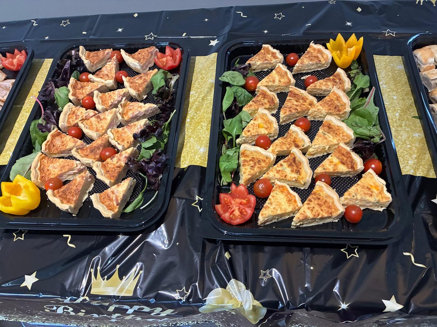 Trays of quiche slices on a bed of salad leaves with cherry tomatoes and peppers